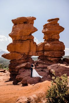 a bride and groom standing in front of large rock formations at the top of a mountain