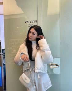 a woman standing in front of a glass wall holding a white purse and looking at the camera