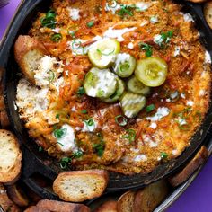 a pizza with cheese and cucumbers on it in a pan next to some bread