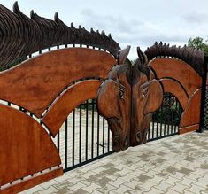 a wooden horse head mounted to the side of a metal fence next to a brick walkway