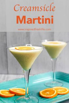 two martinis with orange slices on the rim and one is garnished with creamsice