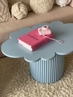 a pink book sitting on top of a blue cloud shaped table next to a couch