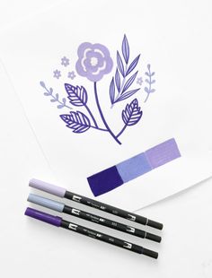 three markers and two pencils sitting on top of a piece of paper next to some flowers