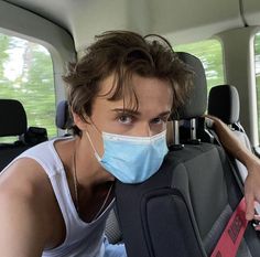 a young man wearing a face mask in the back seat of a car with luggage