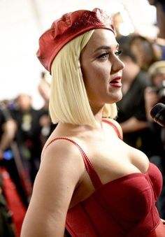 a woman with blonde hair wearing a red dress and headpiece in front of a crowd