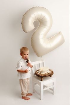 a little boy standing next to a table with a cake and balloon shaped like a question mark