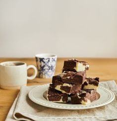 a stack of brownies sitting on top of a white plate next to two cups