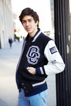 a young man standing next to a pole wearing a jacket with the letter s on it