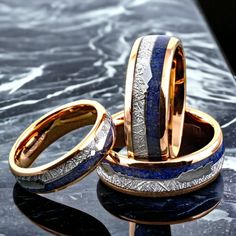 two wedding rings with blue and gold inlays sitting on a marble counter top