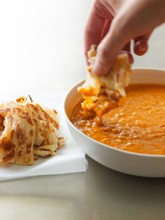 a person dipping cheese into a bowl of soup on top of a white cloth napkin