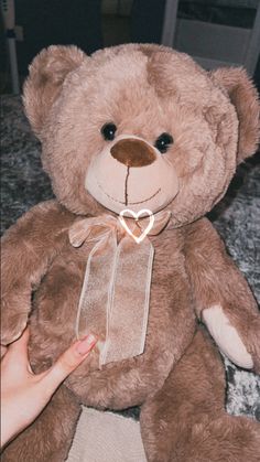 a brown teddy bear sitting on top of a bed next to a person's hand