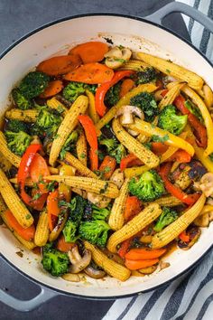 a skillet filled with stir fry vegetables on top of a table next to a striped towel