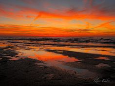 an orange and yellow sunset over the ocean with clouds reflected in the wet beach sand