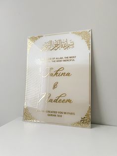 a white and gold wedding card sitting on top of a table next to a vase