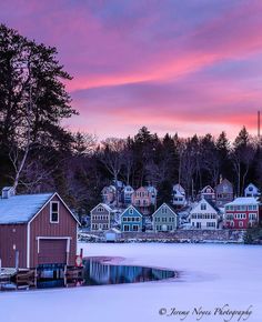 a red house sitting on top of a snow covered field next to a body of water