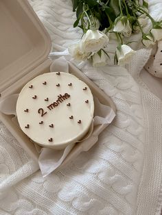 a cake with the word mom written on it sitting in a box next to flowers