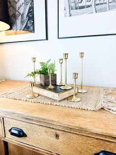 a wooden table topped with two vases filled with plants and candles next to pictures on the wall