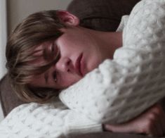 a woman laying on top of a couch covered in a white sweater with her eyes closed