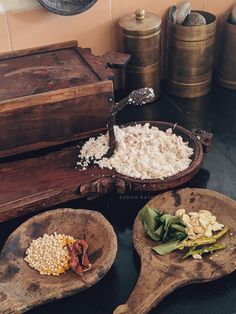 three wooden spoons filled with food on top of a black table next to containers