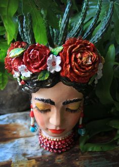 a ceramic head with flowers on it sitting next to some leaves and plants in the background