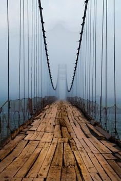 a black and white photo of a bridge with fog in the air over it's sides