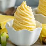 there is a cupcake with yellow frosting on the top and pineapples in the background