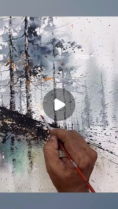 a person is painting with watercolors on a piece of paper that has trees in the background