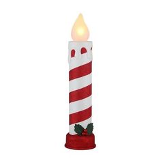 a red and white candle with holly leaves on it's side, lit up