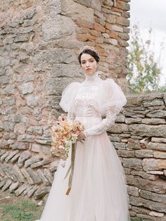 a woman in a wedding dress standing next to a stone wall