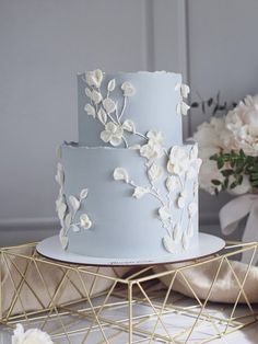 a three tiered cake with white flowers on the side and gold triangles around it