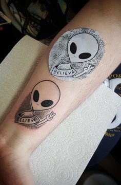 a person with a tattoo on their arm that says believe and an alien holding a coffee cup