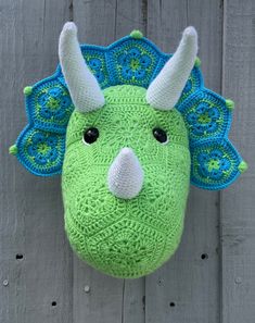 a green stuffed animal with horns hanging on a wooden fence next to it's head