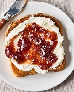 a piece of bread with cream cheese and jelly on it sitting on a plate next to a knife