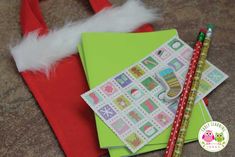 two pencils sitting on top of a green envelope next to a red bag with white feathers