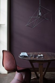 a table with two chairs and a light fixture hanging from it's ceiling in front of a purple wall