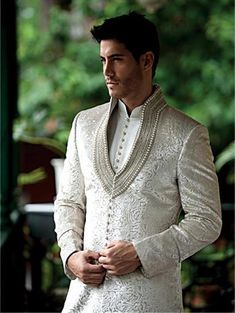 a man in a white suit standing next to trees