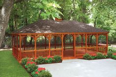 a wooden gazebo surrounded by lush green grass and flowers in the foreground, next to a park bench