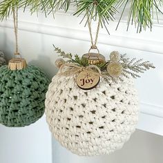 two ornaments hanging from a christmas tree on a mantle with pine needles and twine