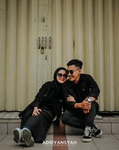 two people sitting on the ground posing for a photo with their arms around each other