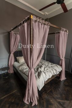 a canopy bed with pink drapes on it in a room that has hardwood floors