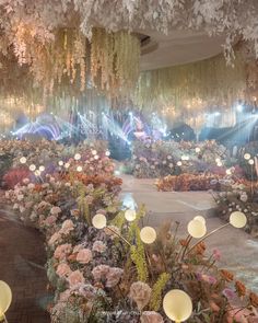 an indoor garden with flowers and chandeliers hanging from it's ceiling, surrounded by lights