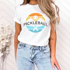 a woman wearing a pickleball t - shirt in front of a white wall