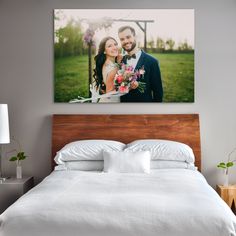 a wedding photo hanging on the wall above a bed in a bedroom with white sheets and pillows