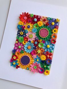 an art piece made out of paper with colorful flowers on the bottom and center, surrounded by smaller ones