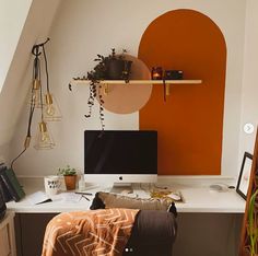 a desk with a computer on top of it next to a chair and potted plant