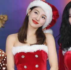 two young women dressed up in christmas outfits and santa hats, one is smiling at the camera