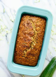 a loaf of zucchini bread in a blue container next to a cucumber