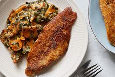 a white plate topped with fish and vegetables next to a fork on a blue plate