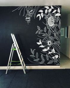 a black wall with white flowers painted on it and a ladder leaning against the wall