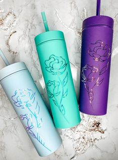 three different colored tumblers sitting next to each other on a marble surface with flowers painted on them